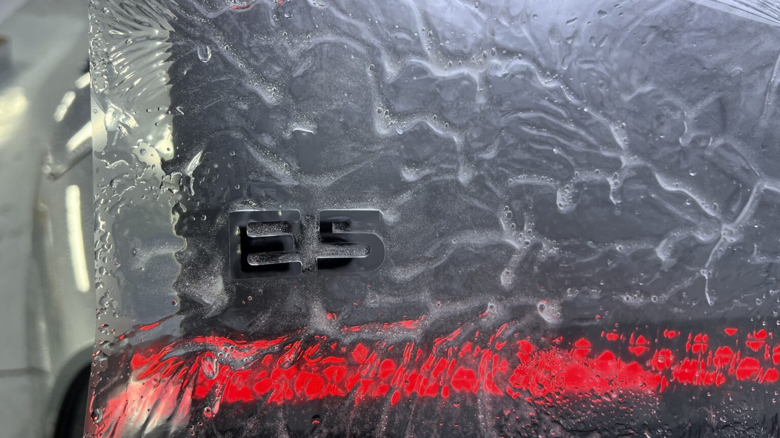 奥迪 E5「E5」字标贴膜特写,可见红色像素尾灯与膜面水珠纹理