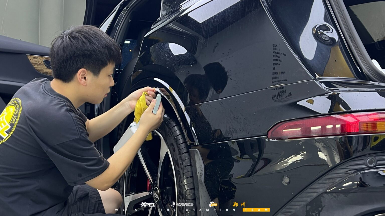技师在奥迪 Q7 前轮拱处贴合膜体,可见黑色湿膜