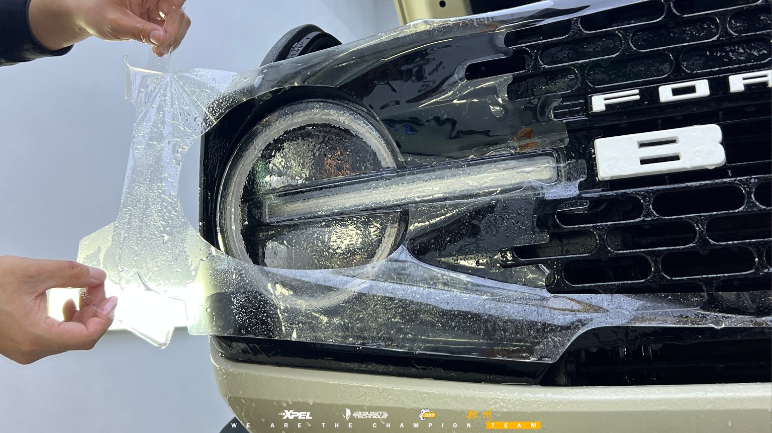 技师在福特烈马前格栅 BRONCO 字标处贴膜，可见湿膜与格栅纹理