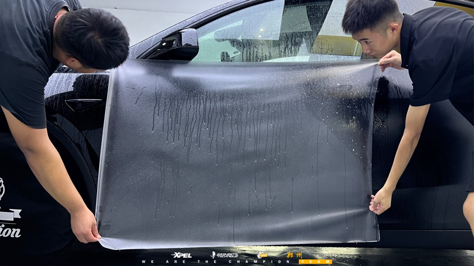 两名技师在特斯拉 Model Y 车身铺展膜体,湿膜大面积可见