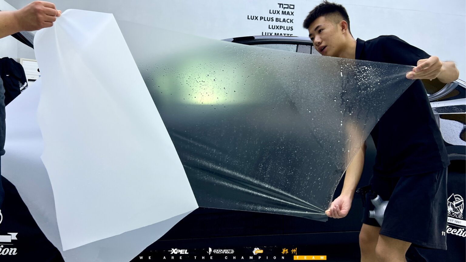 技师在特斯拉 Model Y 后风挡铺展膜体,可见哑光车身质感