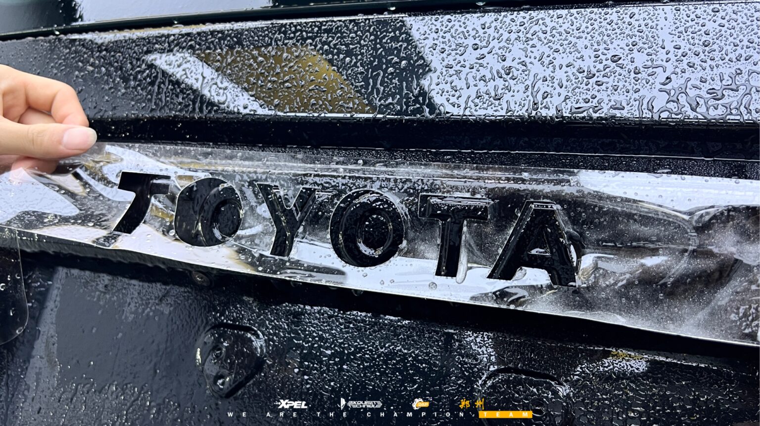 丰田普拉多「TOYOTA」字标贴膜特写，可见湿膜与水痕